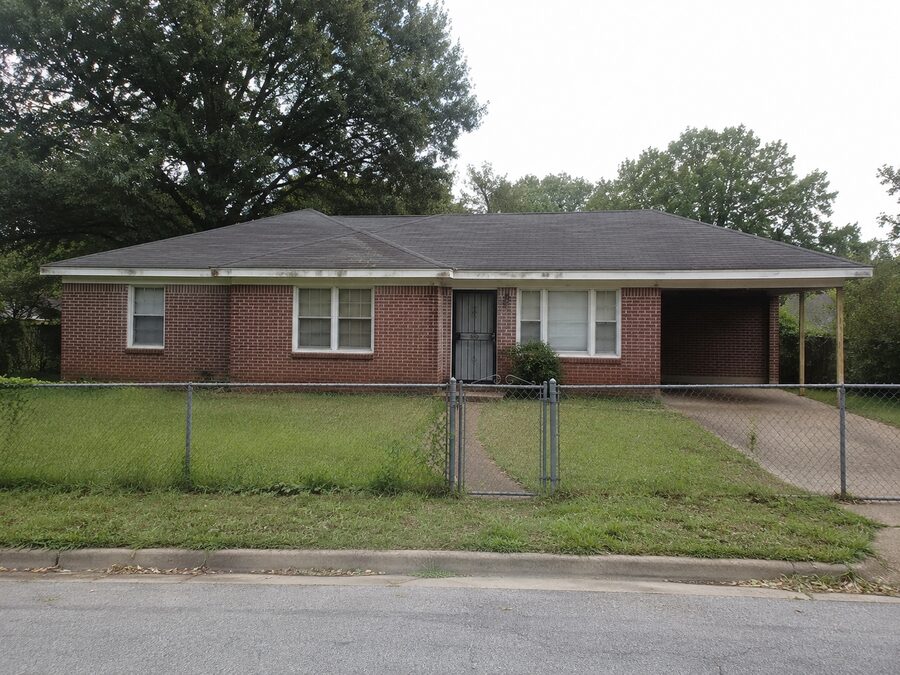A brick ranch house in Memphis behind a chain link fence, photographed on an overcast day.